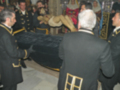 Una imagen de un funeral en una iglesia, con personas vestidas formalmente rodeando a una persona en un ataúd negro.