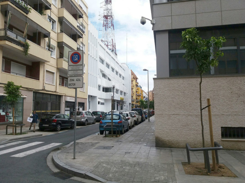 Vista de una calle urbana con edificios, aparcamiento y señal de zona azul sector en el centro.