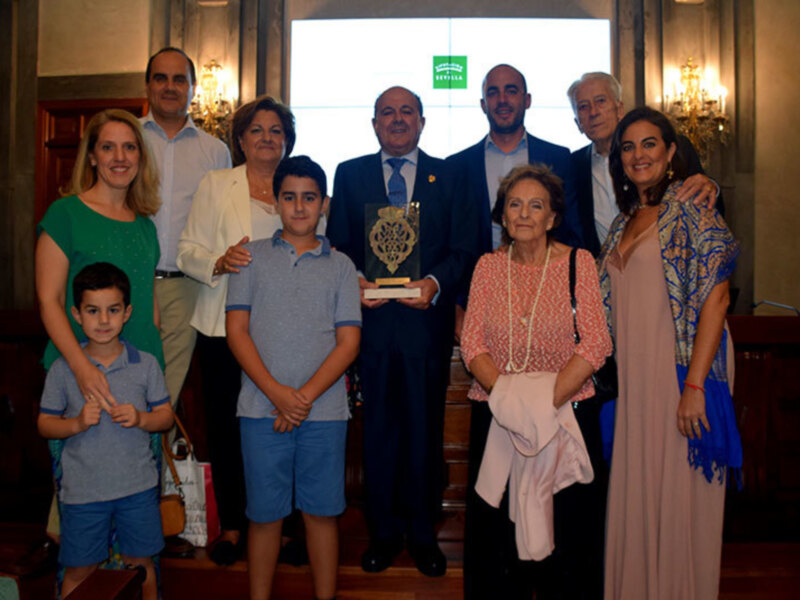 Grupo familiar posando para una foto en un evento formal, con una persona sosteniendo un libro. La familia está vestida formalmente, y el ambiente sugiere una celebración o premiación.