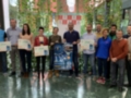 Grupos de personas posan con sus premios y un cartel promocional, frente a una pared verde.