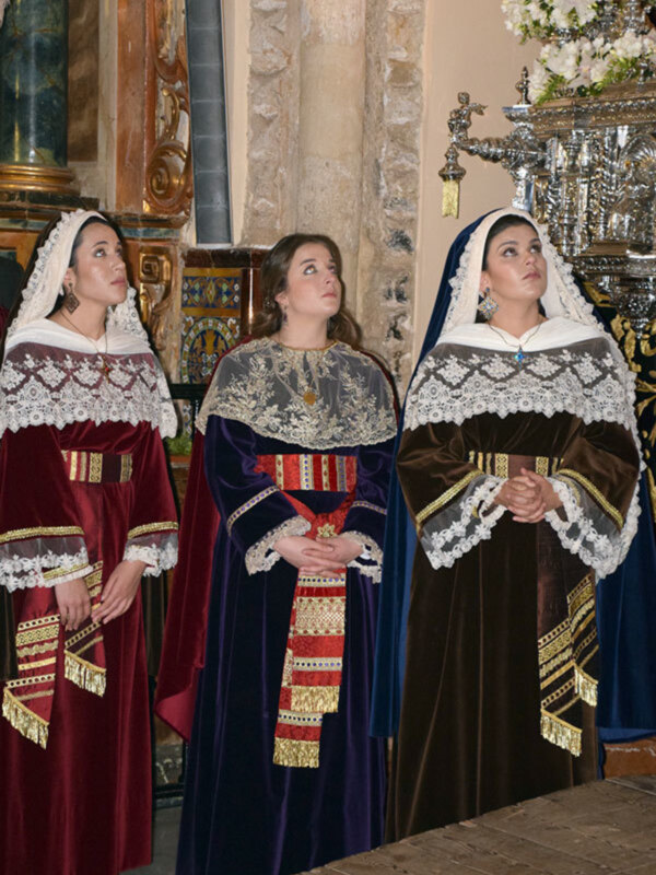 Tres mujeres vestidas con trajes tradicionales de la región, posando en una iglesia con detalles arquitectónicos.