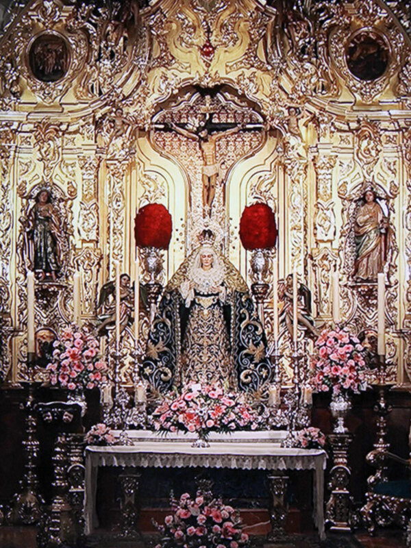 Altar con estatuas religiosas y flores en un ambiente de iglesia.