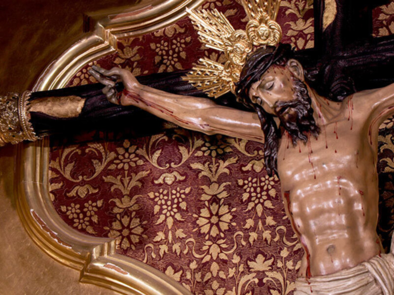 Escultura de Cristo crucificado en una pared decorada con motivos florales.