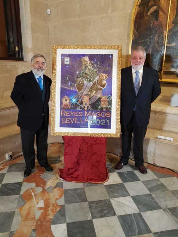 Dos hombres en trajes posan junto a un póster de Reyes Magos 2021 en Sevilla. La imagen está ambientada en un entorno con decoración clásica y marmolados.