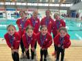 Equipo de nadadores femeninos posando con medallas en una piscina interior.