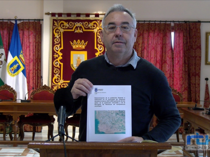 Un hombre sostiene un documento en una sala de conferencias con banderas y cortinas rojas.