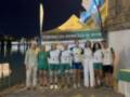 Equipo de remo celebrante en el mar nocturno, con una bandera de la Federación Andaluza de Remo en el fondo.
