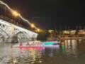Noche de remo bajo el Puente de Triana, Sevilla, con luces y espectadores en el puente.