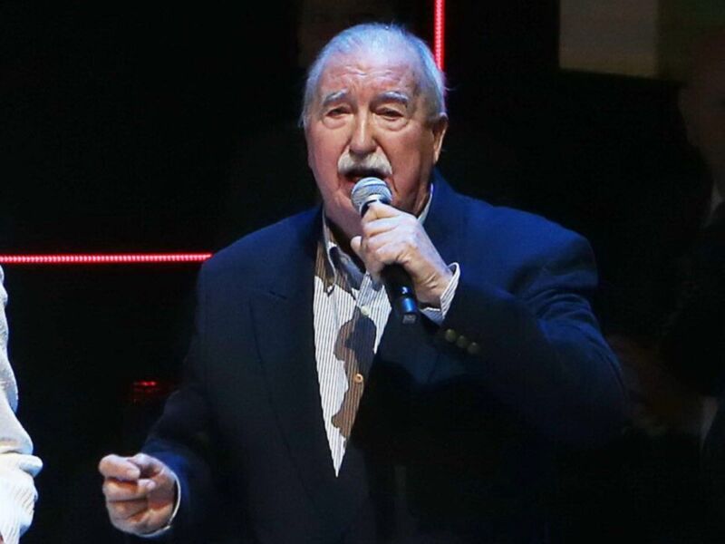 Senior man singing into a microphone on stage.