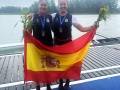 Dos atletas españolas posan con la bandera de España y medallas, celebrando un logro deportivo.