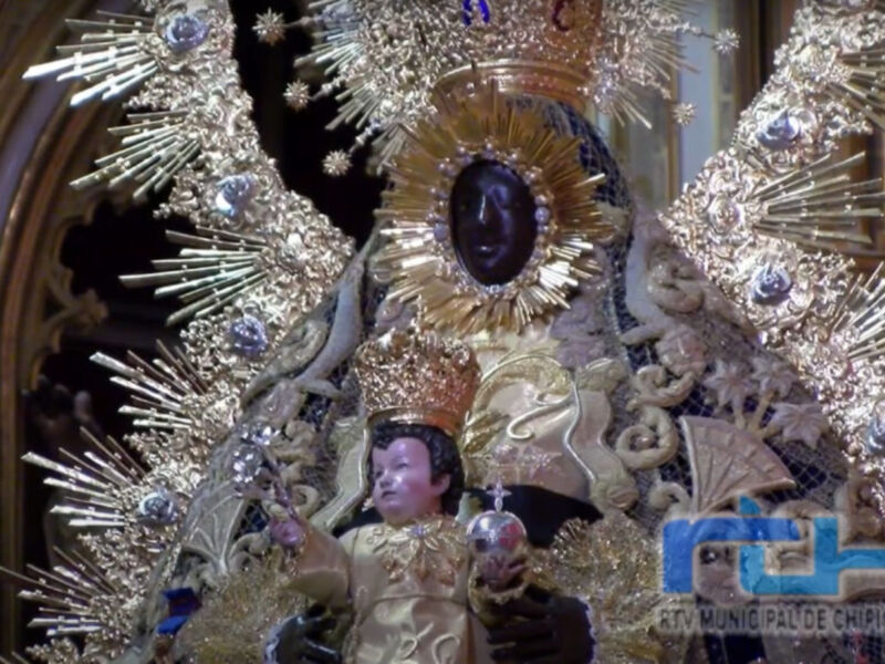 Imagen de la Virgen María con un halo dorado y joyas, en una iglesia.