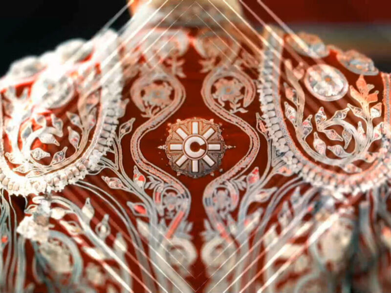 Detalle de una vestimenta ceremonial con bordados en tonos rojos y dorados, probablemente parte de una vestidura religiosa o ceremonial.