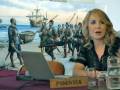 Una mujer en un entorno de conferencia frente a una pantalla que muestra una escena histórica con marineros y un barco en el fondo.