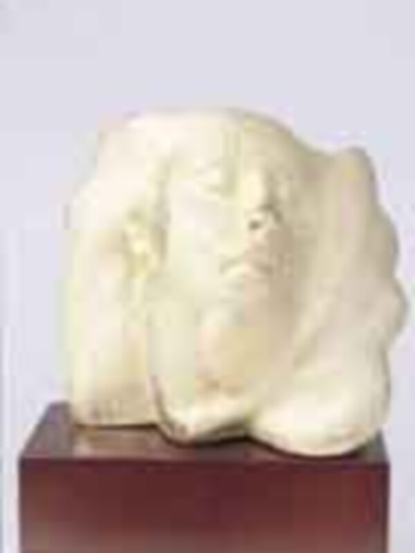 Escultura en blanco de una cabeza humana, posiblemente representando un rostro humano. La escultura está sobre un pedestal de madera, con detalles en blanco y negro.