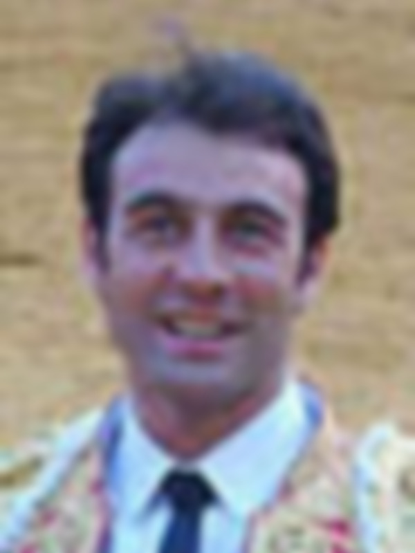 Un hombre con una camisa de manga larga y un sombrero, posando frente a un paisaje montañoso.