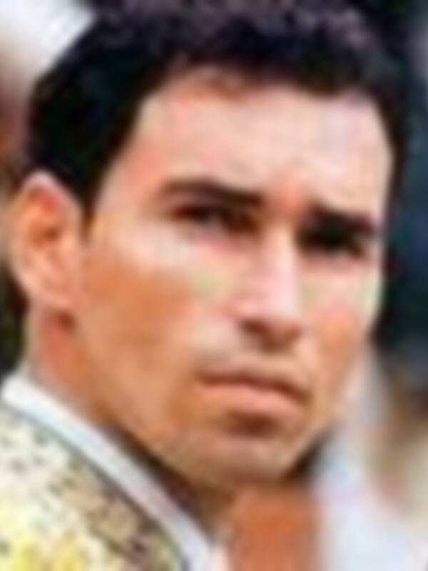 Un hombre con una camisa de cuadros rojas y negras, posando con un sombrero en la cabeza.