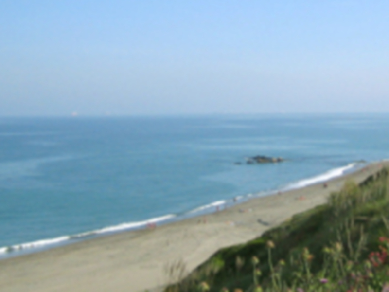 Playa con arena blanca y agua azul, montaña en el horizonte.
