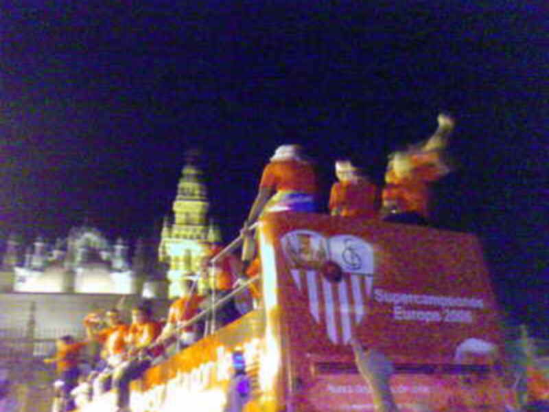 Un grupo de personas disfruta de una noche en el estadio, con una estructura roja que parece ser parte del escenario de un evento deportivo. La iluminación nocturna y la presencia de una torre en el fondo añaden un ambiente festivo a la escena.