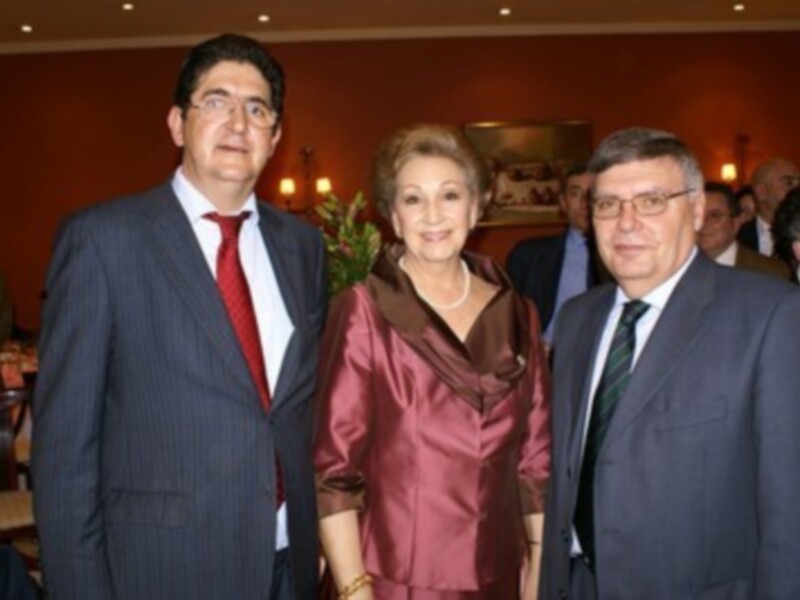 Tres personas en trajes formales posando juntos en un evento social o profesional.