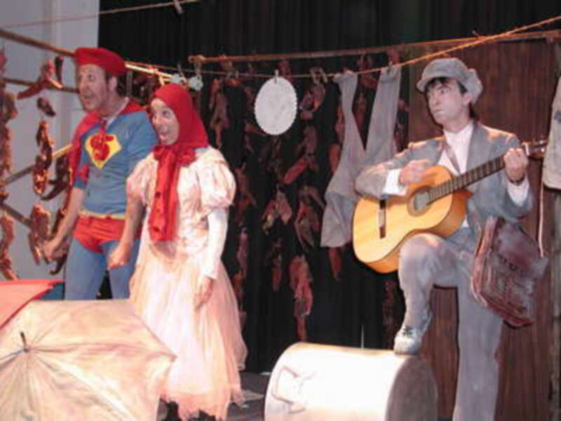 Actores en escenario interpretando una escena teatral con música y vestimenta variada.