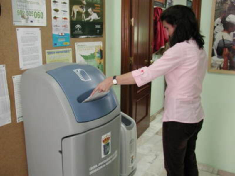 Una persona depositando un recibo en un cajero automático de la banca. El cajero tiene un logotipo de la entidad financiera y está ubicado en un entorno interior con carteles informativos en la pared.