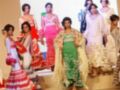 Una modelo con vestido verde y flecos se encuentra en el centro de la imagen, mientras que otras modelos presentan vestidos tradicionales españoles. La escena se desarrolla en un escenario con una pantalla de fondo que muestra imágenes de modelos.