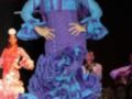 Una modelo presenta un vestido de flamenca con detalles en azul y púrpura, en un desfile de moda.