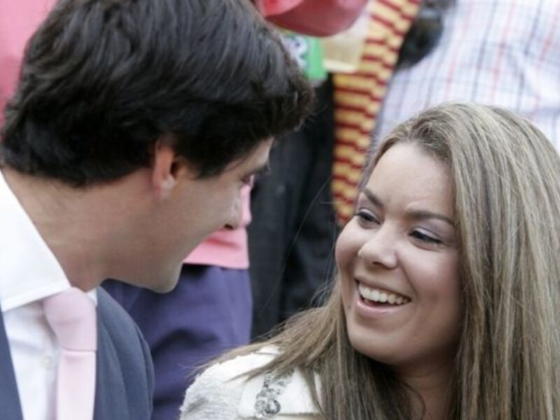 Imagen muestra a una joven sonriendo y mirando a un hombre, ambos están en un ambiente festivo con globos de colores al fondo.