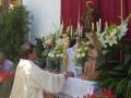 Un sacerdote bendice una mesa decorada con flores y estatuas religiosas durante una celebración religiosa.
