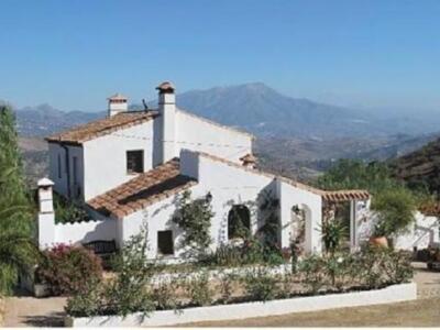 Elegante casa colonial con techo de tejas rojas y chimeneas blancas, rodeada de vegetación y con un hermoso paisaje montañoso en el fondo.