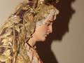 Estatua religiosa de una virgen con vestimenta dorada y joyas, llevando un halo y corona. La imagen muestra la parte superior de su rostro y vestimenta elaborada, con detalles en oro.