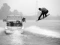 Un hombre realiza un salto de wakeboard en el agua, con una barca detrás.