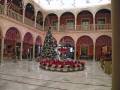 Interior de un patio decorado con árbol de Navidad y flores, con arcos y balcones en un ambiente festivo.