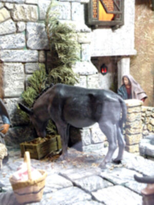 Representación de la natividad con burro y figura humana en un entorno de piedra y paja.