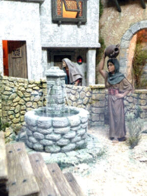 Figura histórica en escena medieval, con mujer levantando jarra cerca de pozo.