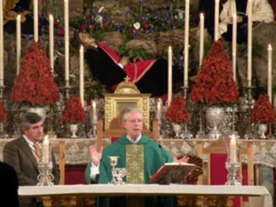 Un sacerdote oficia una misa en una iglesia adornada con flores y velas.