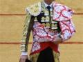 Un torero en traje de luces con abrigo rojo y dorado, sosteniendo un sombrero en una mano.