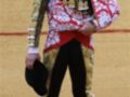 Un torero en traje tradicional, con chaqueta de color dorado y rojo, pantalones negros con detalles dorados y calcetines rosas.
