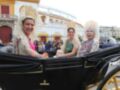 Tres mujeres en trajes tradicionales andaluces montan en un carruaje negro y dorado, frente a una plaza de toros. La imagen transmite un ambiente festivo y cultural típico de Andalucía.