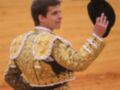 Un torero en traje de luces saludando con el sombrero en un ruedo de arena.