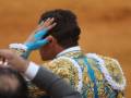 Un torero en traje tradicional de color azul y dorado con detalles blancos, ajustando su gorro mientras prepara para el toro.