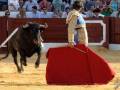 Un torero se enfrenta a un toro en una corrida de toros, con el público en el fondo.