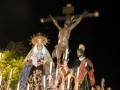 Cruz de Cristo en procesión nocturna, con la Virgen de la Soledad y el Cristo de la Misericordia, iluminados por velas y con un fondo oscuro.