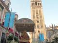 Fotografía captura una procesión religiosa en Sevilla, con un carro de flores y banderas frente a la Giralda.
