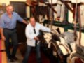 Dos hombres posan junto a varios asientos de caballo en una tienda. El ambiente es acogedor con muebles y decoración típica de un establecimiento dedicado a la venta de equipamiento para caballos.