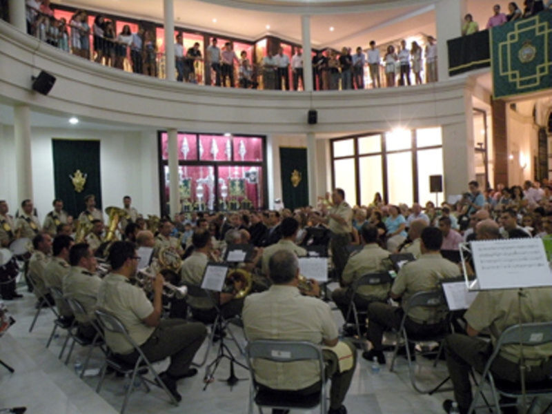 Concierto de banda militar en un salón circular con público en las gradas y músicos en formación.