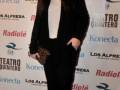Elegante mujer posando en la alfombra roja de un evento de teatro, con un look sofisticado en negro y blanco, y un fondo de patrocinadores.