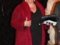 Una mujer con una chaqueta roja larga y un vestido negro, sosteniendo una botella de champán.
