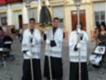 Cuatro personas vestidas con trajes blancos y negros, posiblemente en una procesión religiosa o festiva.