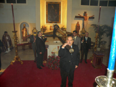 En una iglesia, un hombre toma una foto en el centro de la imagen. A su alrededor, hay personas vestidas formalmente y una cruz en el fondo. La decoración incluye flores, velas y un altar con una imagen religiosa en el fondo.